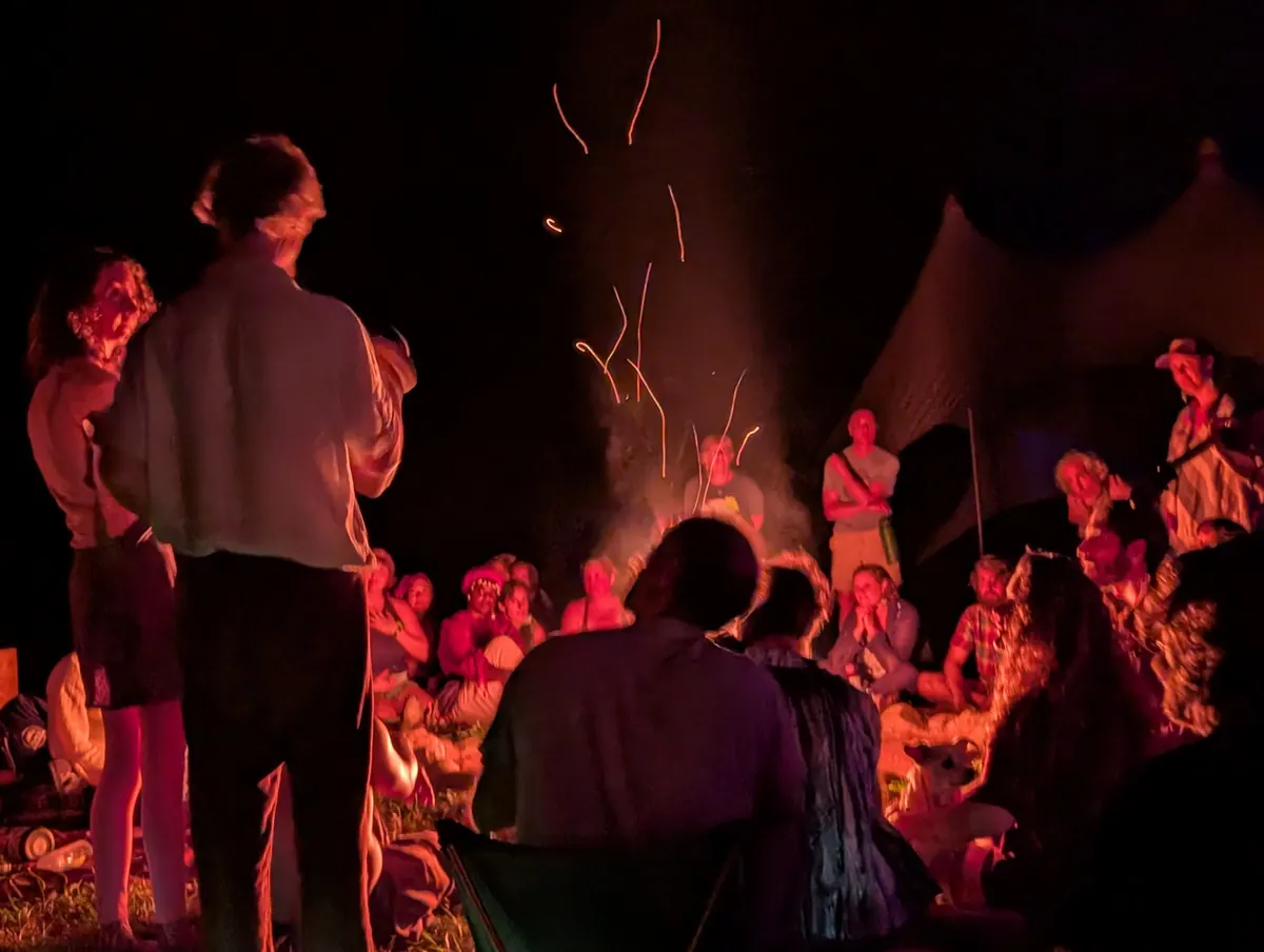 Singing around the fire at Love Song, with sparks rising and everyone lit red by the flames