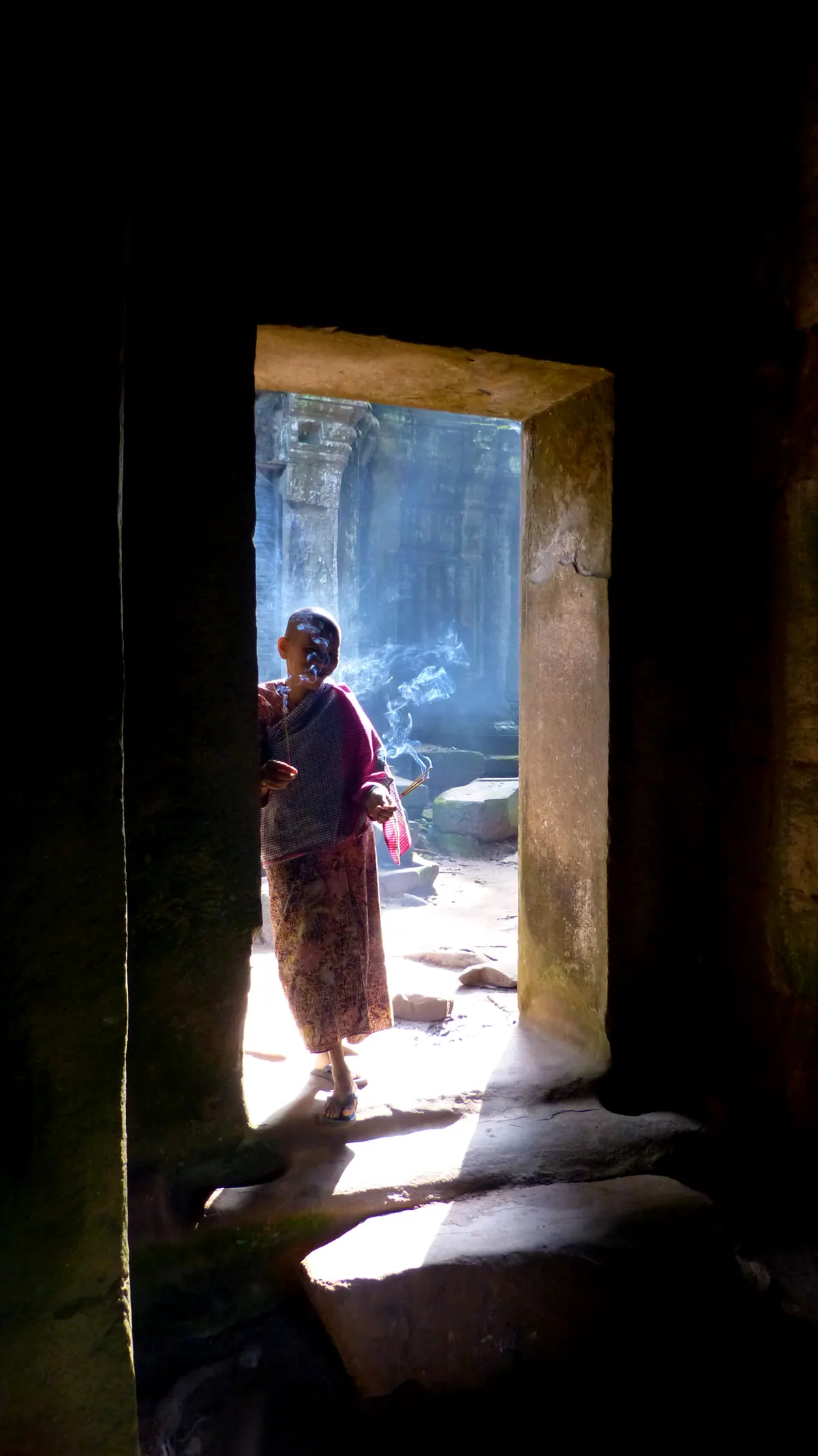 A monk silhouetted in a bright doorway inside a dark Angkor temple