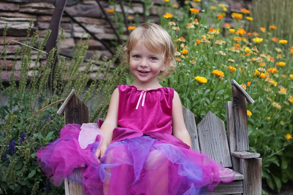 A little girl in a pink dress, backlit among wildflowers