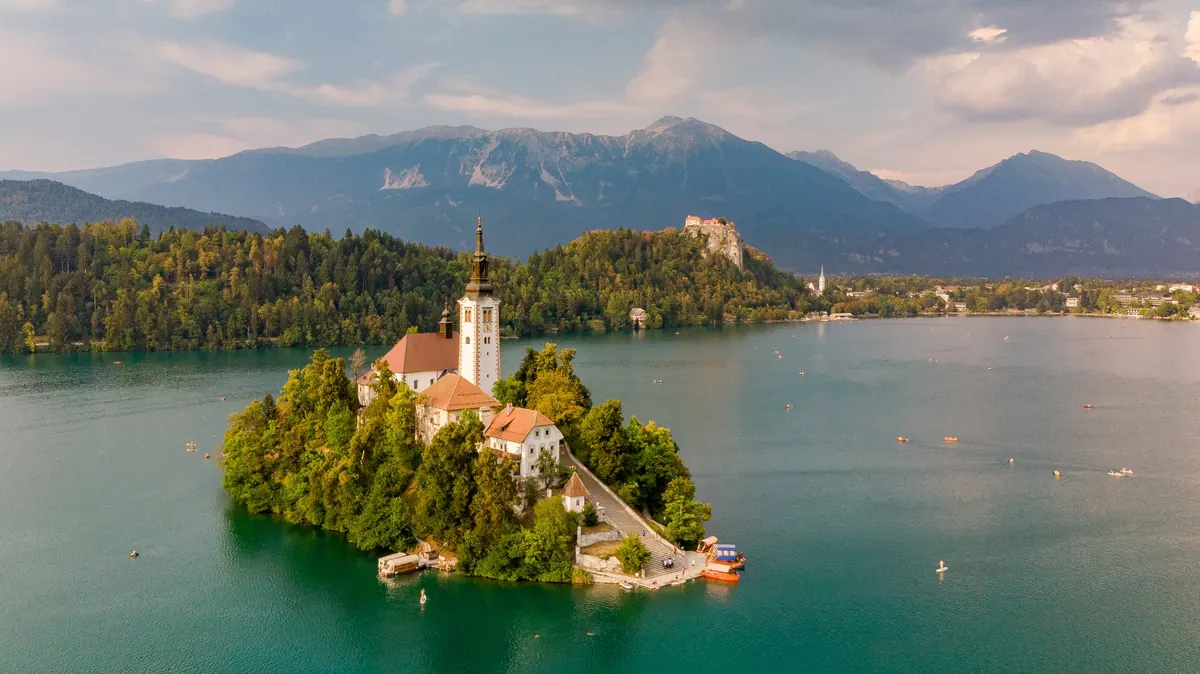 Lake Bled's island church from the air, with the clifftop castle and Julian Alps beyond, Slovenia