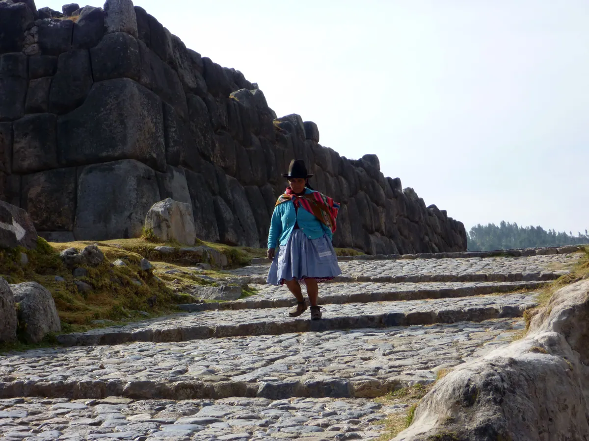 A woman in traditional dress walking a stone lane above Cusco