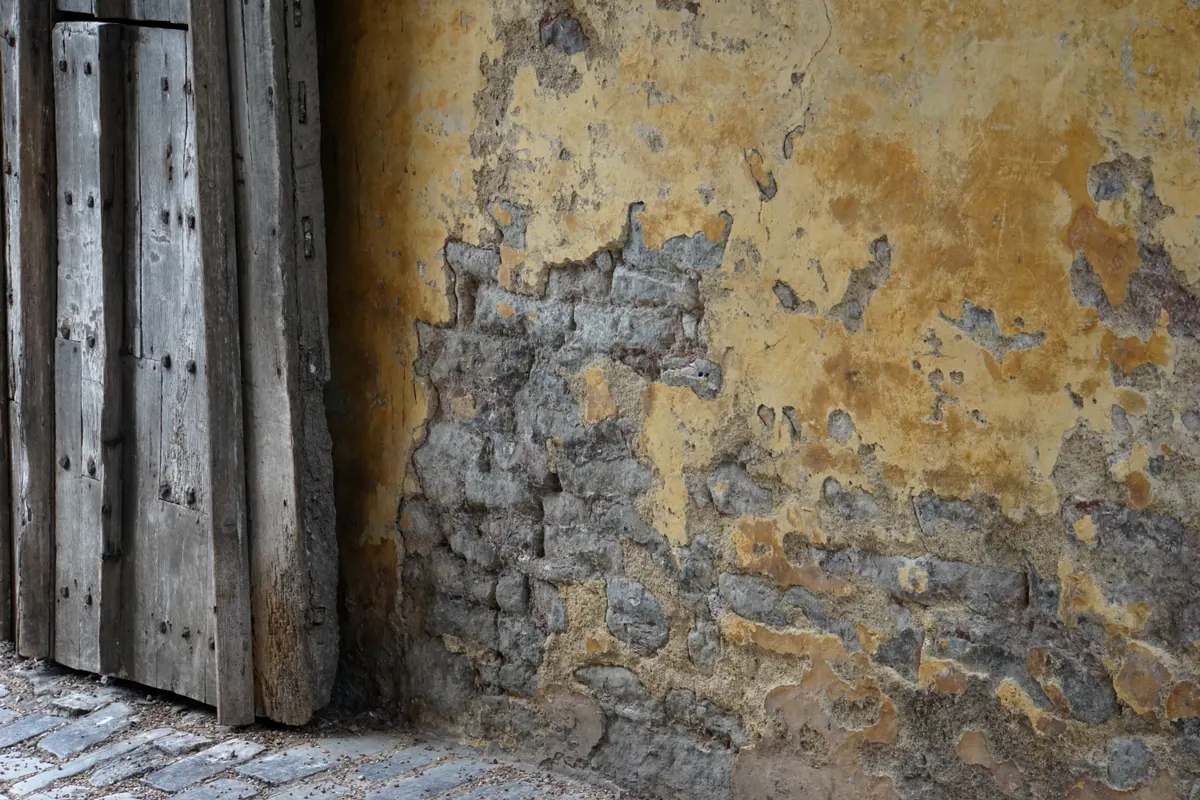 Layers of weathered plaster and stone beside an old wooden doorway