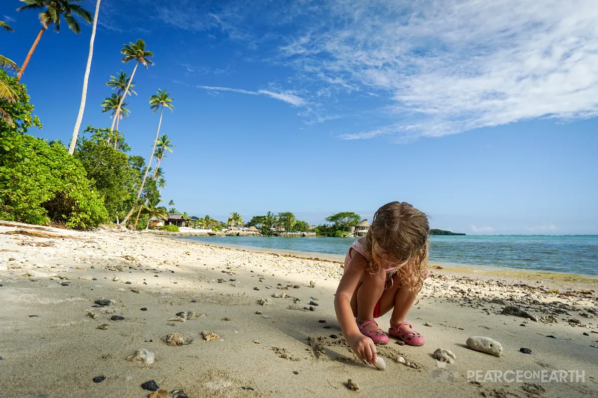 A child drawing in pale sand beneath palms on a quiet Fijian beach