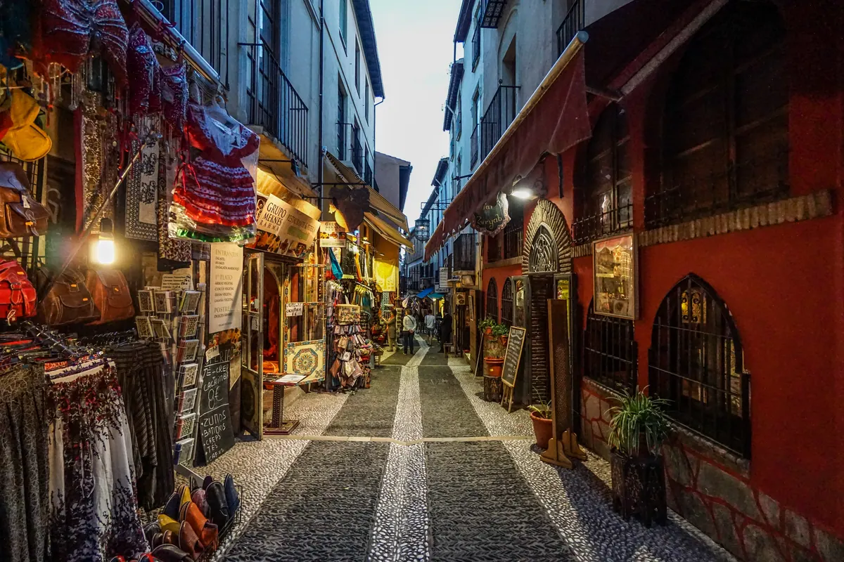 A narrow Granada market lane glowing with lamps, textiles, and painted walls