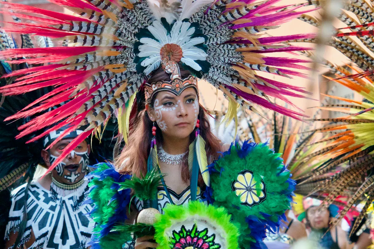 A dancer in a vivid feathered headdress and painted face during an Indigenous dance procession