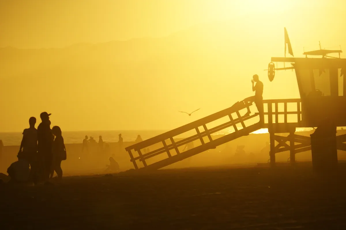 Silhouetted figures and a lifeguard tower in thick golden haze at sunset, Venice Beach