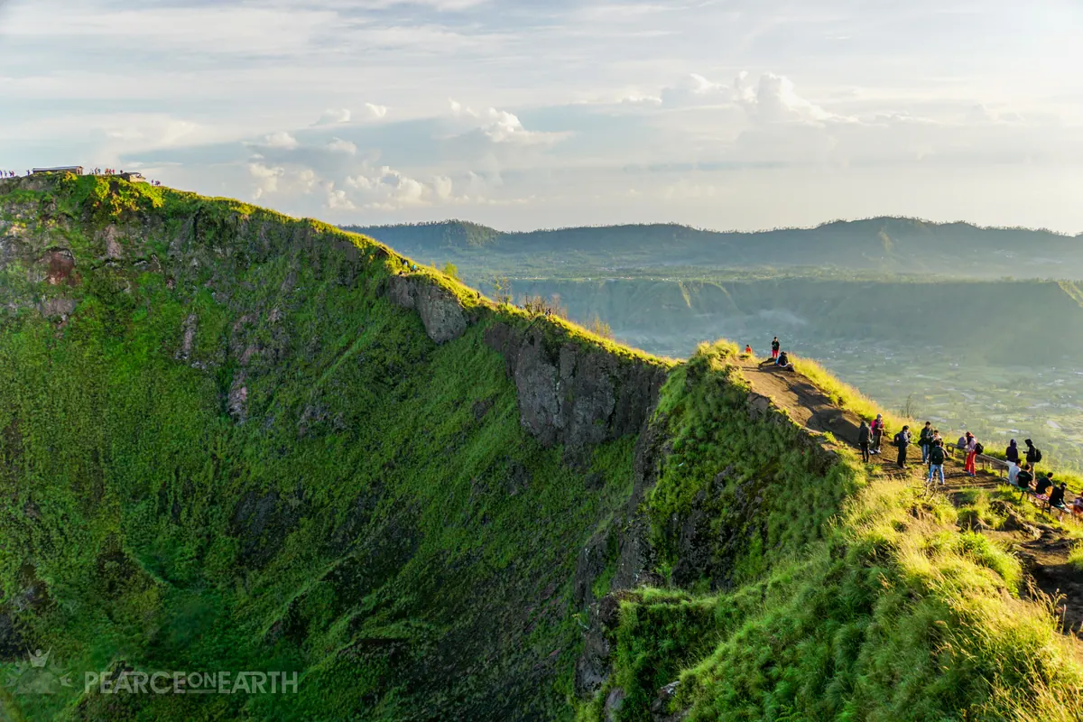 Hikers following the green rim of Mount Batur above a misty caldera