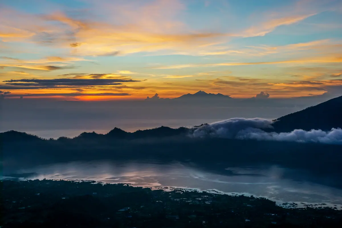 A fiery sunrise above Mount Batur, clouds, and the lake-filled caldera
