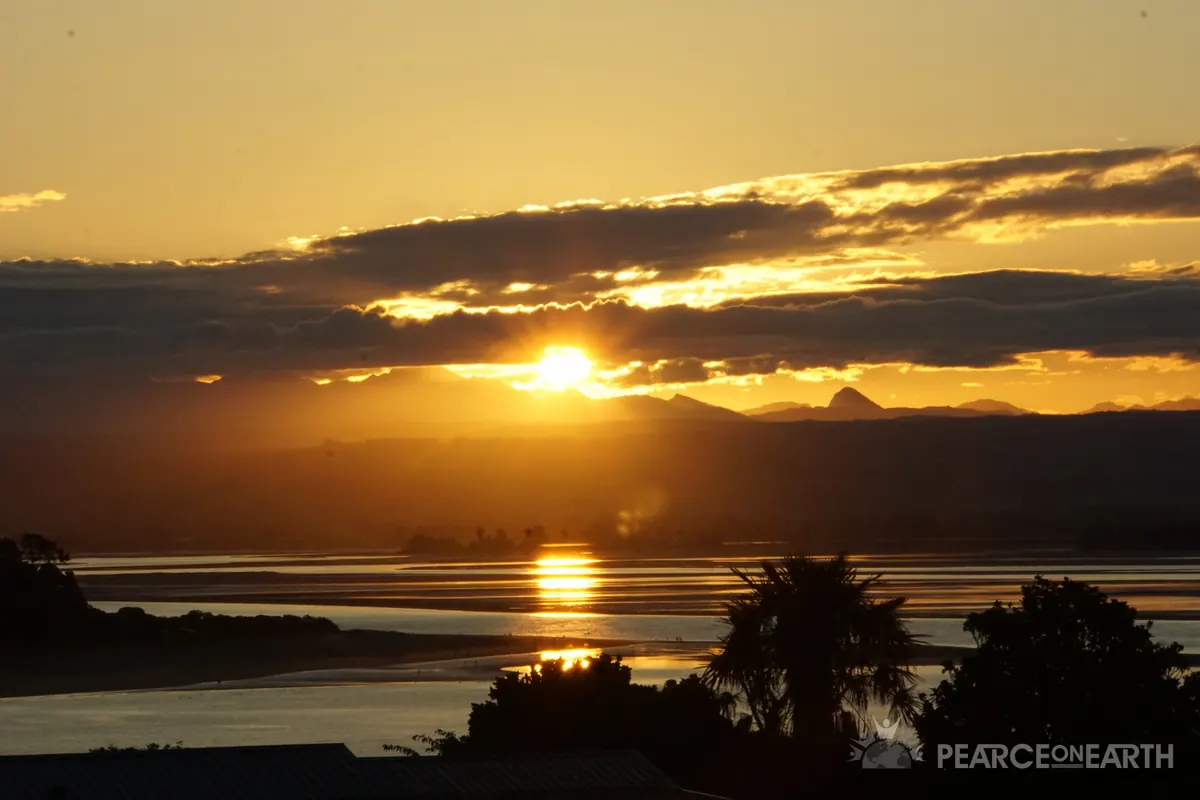 The setting sun mirrored in the water beneath layered clouds
