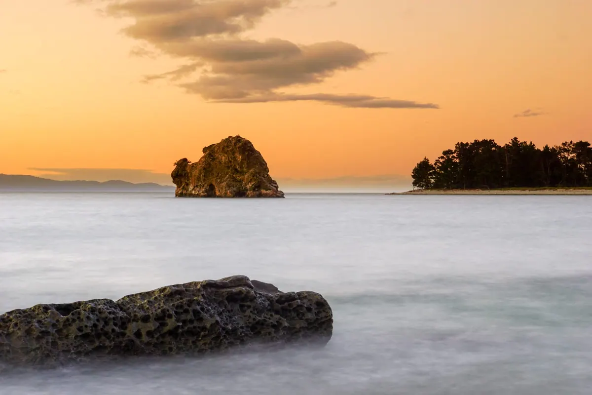 Silky long-exposure sea around a lone rock at dusk