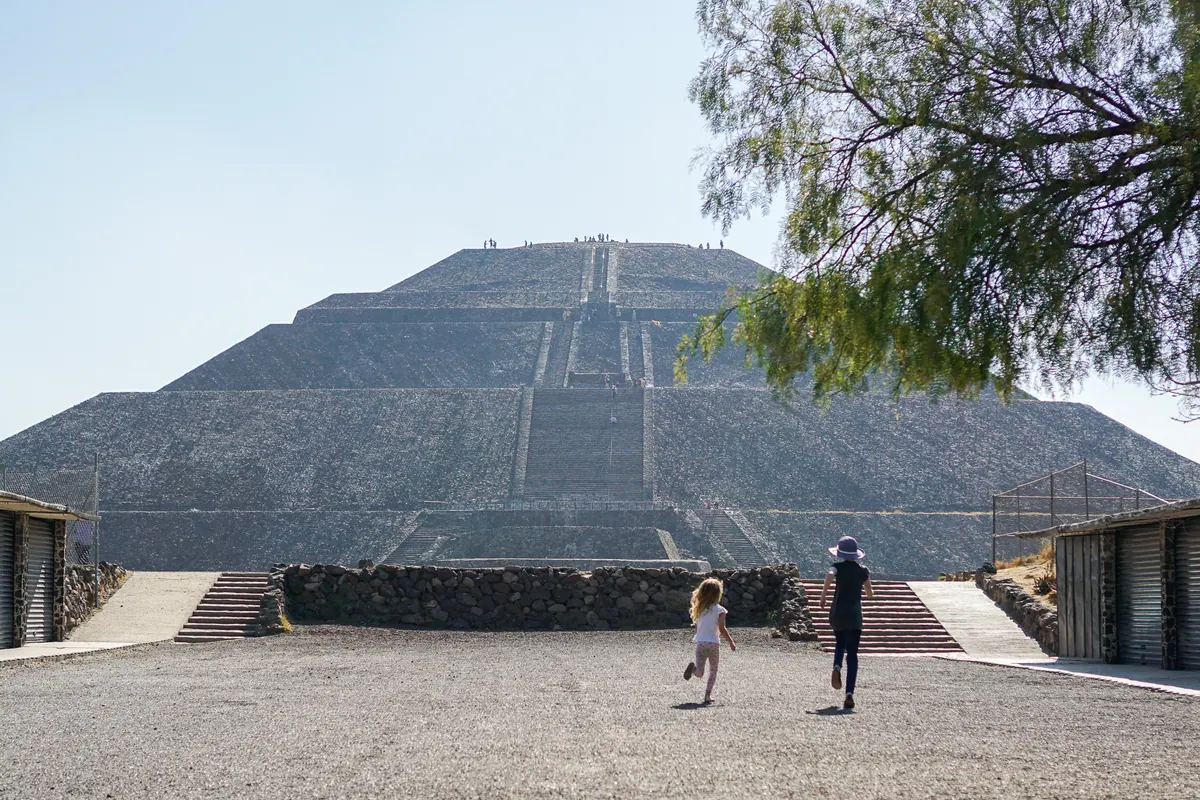 Two children running across the gravel toward the Pyramid of the Sun at Teotihuacán
