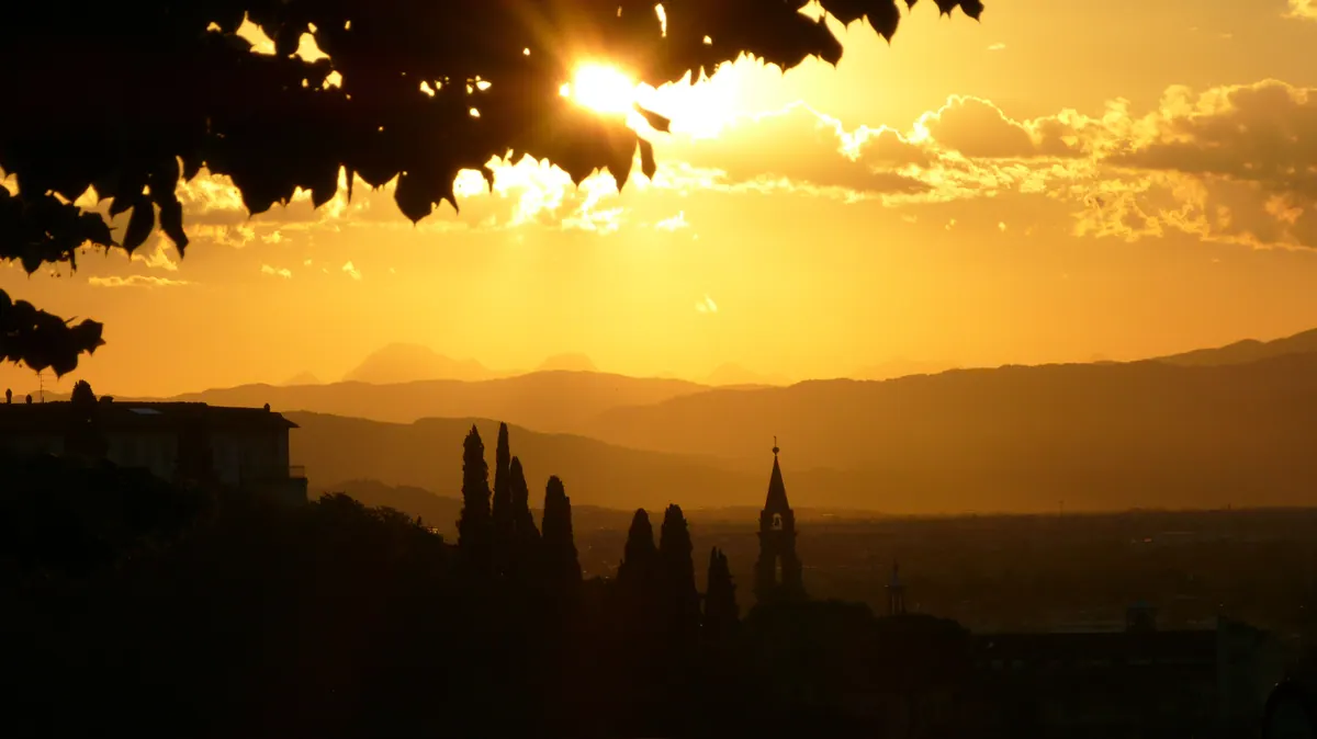 Golden light breaking over layered Tuscan hills and a distant bell tower