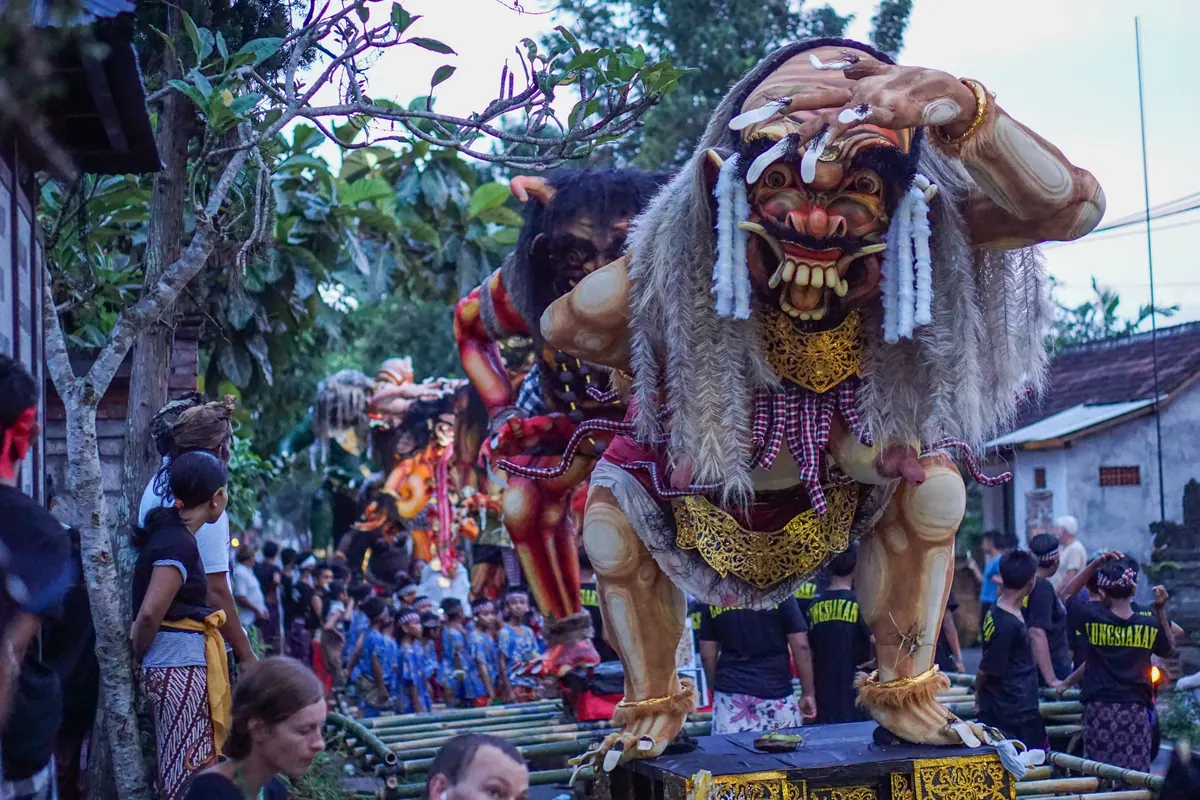 A towering ogoh-ogoh figure carried through a crowded festival in Ubud